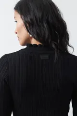 Polera de tejido acanalado color negro, con cuello alto y puños con terminación de volados. Presenta un diseño entallado y textura vertical.