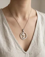 Dije circular de acero inoxidable con diseño calado de dos mariposas en el centro y detalle de guarda griega en el borde.