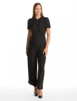 Enterito de seda fría color negro, con cuello a la base fruncido, escote en V con botones metálicos y detalle plisado vertical en el frente. Presenta mangas cortas con terminación fruncida, cintura con lazo de ajuste y pantalón de pierna ancha con caída fluida.