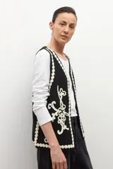 Chaleco tejido negro con escote en V, sin mangas y bordados en color crema con motivos florales y detalles de ondas en los bordes.