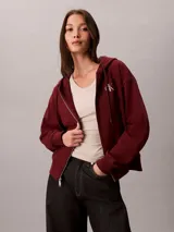 Campera canguro Calvin Klein de felpa color bordó, con capucha ajustable por cordones, cierre frontal completo de cremallera, mangas largas y bolsillos laterales. Presenta el logo monograma de la marca bordado en el pecho.