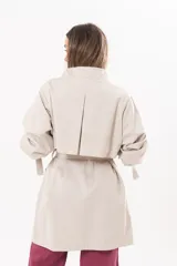 Trench de gabardina Tencel color beige, de silueta relajada, con cierre frontal de botones, lazo desmontable y regulable en la cintura, bolsillos amplios y lazos en los puños.