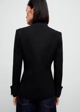 Chaqueta negra de estilo militar entallada, con cuello mao, cierre frontal de botones dorados con efecto joya y manga larga con trabillas y puños abotonados.