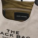 Bolso tipo hobo de Marc Jacobs, modelo The Belted Sack, confeccionado en lona color beige con detalles en cuero marrón. Presenta el logo de la marca grabado en el frente y una forma relajada con cierre ajustable.