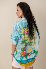 Camisa de manga larga con estampado tropical, fondo a rayas celestes y blancas, cuello camisero y cierre frontal de botones.