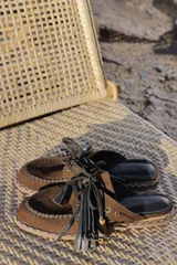 Suecos de cuero marrón con diseño artesanal, costuras visibles, cordones y flecos XL decorativos.