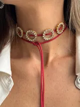 Gargantilla choker con cordón rojo y dijes circulares dorados con strass. El cordón se ata en la parte delantera.