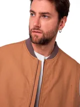 Chaleco de trabajo Caterpillar en color tostado, confeccionado en lona resistente. Presenta cierre frontal completo, cuello tipo bomber en tejido acanalado, bolsillos frontales tipo parche y etiqueta de la marca en el pecho.