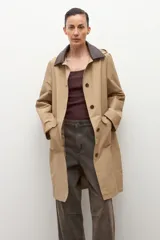 Trench impermeable color beige con cuello camisero en contraste de color marrón oscuro. Presenta cierre frontal con botones, bolsillos delanteros con solapa y mangas largas.