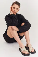 Sandalias de plataforma plana con diseño de tiras cruzadas en tonos beige y marrón. Presentan una base negra, puntera cuadrada y cierre con hebilla metálica lateral.