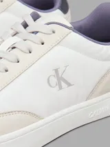 Zapatillas de corte bajo Calvin Klein, con diseño minimalista en color blanco y beige. Presentan una combinación de materiales en la capellada, incluyendo piel y ante, con detalles en contraste en el talón y logo de la marca en el lateral y la mediasuela.