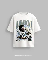 Remera blanca de algodón premium de alto gramaje, con estampa frontal que incluye imágenes de Diego Maradona besando la Copa del Mundo y jugando al fútbol, con el texto "MARADONA" en tipografía grande.