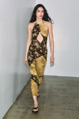 Vestido largo de viscosa con estampado floral y diseño de paneles diagonales en tonos tierra. Presenta cuello halter con cierre de botones y abertura frontal en el pecho, dejando los hombros al descubierto.