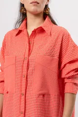 Camisa larga amplia color coral con patrón a cuadros, cuello camisero, cierre frontal con botones y grandes bolsillos en el pecho.