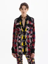 Camisa de manga larga con estampado floral sobre fondo negro. Presenta cuello, cartera de botones, puños y canesú en color negro liso. Tiene dos bolsillos plaqué con tapa en el frente, asegurados con broches metálicos negros grabados.