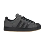 Championes Adidas Superstar ST de estilo urbano, confeccionados en gamuza gris con las icónicas tres tiras laterales en negro. Presentan la clásica puntera de goma, cordones negros y una suela de goma con base color caramelo.