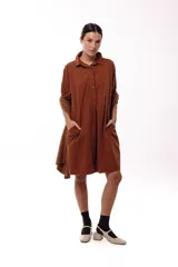 Vestido corto de silueta amplia y fluida, color marrón chocolate. Presenta cuello camisero, cierre frontal parcial con botones y bolsillos laterales. Su diseño holgado y versátil permite usarlo como vestido o sobreprenda.