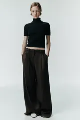 Pantalón de tiro medio con pinzas en el delantero, trabillas para cinturón, bolsillos laterales y tapetas decorativas en la parte trasera. Presenta un cierre frontal con cremallera, botón interior y gancho metálico.