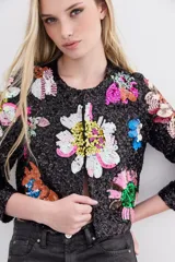 Saco corto de lentejuelas negras con bordados florales multicolores hechos a mano. Presenta cuello redondo, mangas largas y cierre frontal con ganchos invisibles.