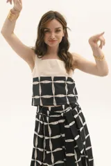 Top de tirantes anchos con diseño bicolor, presentando una parte superior en color crudo y una parte inferior estampada con un patrón geométrico de cuadrícula en negro y blanco.