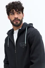 Campera de felpa color camel con cierre frontal, capucha ajustable con cordones negros y bolsillos laterales con cierre negro. Presenta un estampado pequeño en el pecho con texto en color oscuro.