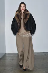 Chaqueta bomber negra de corte corto y diseño abullonado, con cuello de solapa amplio en pelo sintético marrón. Cuenta con mangas largas y cierre frontal.