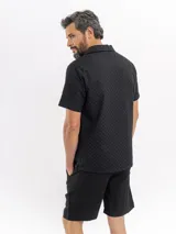 Camisa de manga corta color negro con sutil patrón tipo damero, cuello cubano y cierre frontal con botones.