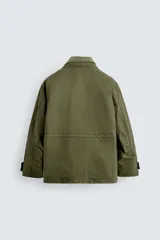 Cazadora de estilo militar en color verde oliva, confeccionada en algodón con efecto lavado. Presenta un diseño de corte relajado con cuello doble, cierre frontal con cremallera oculta por solapa con botones a presión, cuatro bolsillos frontales de plastrón con solapa y puños ajustables con botón.