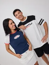 Remera azul marino de algodón con mangas cortas raglán blancas con ribete naranja y estampado ovalado con el logo de Rusty en el pecho.