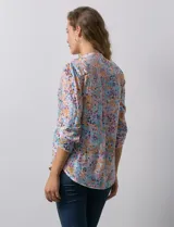 Blusa de gasa estampada con flores en tonos rosa, amarillo y azul. Tiene cuello a la base, escote en V y botones. La delantera tiene detalle plisado y las mangas son 3/4 regulables con presilla y botón.