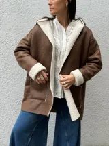 Tapado de eco cuero gamuzado color marrón con interior y bordes de corderito sintético color crema. Presenta diseño con capucha, bolsillos frontales y corte relajado.