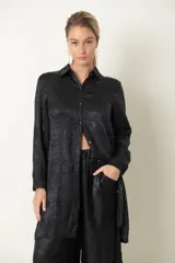 Camisa plateada de poliéster con textura metalizada, corte amplio, cuello clásico, cierre frontal con botones y mangas largas con puños abotonados.