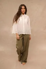 Camisa blanca de manga larga con diseño oversize, cuello camisero y cierre frontal de botones. Presenta detalles de bordado inglés calado en el ruedo y en los puños acampanados.