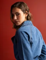 Chaqueta larga de jean azul con cuello con solapa, abertura central con botones, bolsillos delanteros, cintura con pasadores y lazo de ajuste, y puños con botón.