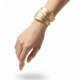 Pulsera rígida envolvente de cuero dorado con textura granulada, diseño en espiral que imita la forma de hojas superpuestas alrededor de la muñeca.
