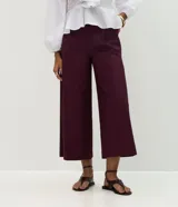 Pantalón tipo pantacourt de sastrería en color bordó, con pliegues delanteros, cintura con trabillas y cierre frontal. Presenta un corte amplio y sofisticado, e incluye un cinturón fino desmontable.