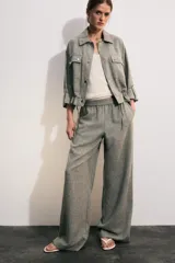 Chaqueta corta gris de tejido texturizado con cuello solapa, manga larga con trabilla, bolsillos delanteros con solapa y cierre frontal de botones metálicos.