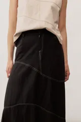 Falda larga de lino color beige, de corte asimétrico con costuras decorativas pespunteadas en contraste y diseño envolvente con bajo más largo en la parte trasera.