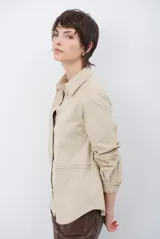 Camisa de estilo casual confeccionada en material tipo gamuza color marrón, con cuello clásico, cierre frontal con botones y costuras a la vista en tono contrastante.