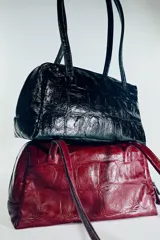 Bolso de hombro de piel con formato bowling, acabado texturizado tipo cocodrilo y color bordó. Cuenta con doble asa de hombro, cierre principal de cremallera con doble tirador y bolsillo interior con cremallera.