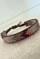 Pulsera tejida artesanalmente con cuentas Miyuki en una paleta de colores que combina tonos beige, marrones, bordó y oro rosa. Presenta un diseño ajustable mediante un cordón marrón.