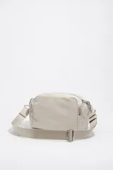 Bolso tipo morral Bimba y Lola, de color tostado, confeccionado en nylon suave con detalles en cuero y tirantes de cordón. Cuenta con múltiples compartimentos con cierre y el logo metálico de la marca en el frente.