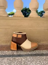 Botinetas de cuero en combinación tricolor de marrón, tostado y beige, con plataforma y taco ancho de madera. Cuenta con detalle de tira con hebilla en el lateral y cierre interno.