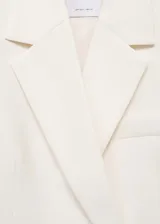 Blazer de corte recto y diseño estructurado, color crema, con cuello de solapa con muesca y cierre frontal de doble botonadura con botones en contraste. Cuenta con dos bolsillos de ribete frontales y mangas largas.