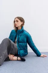 Campera puffer metalizada color azul petróleo, con cuello alto, cierre frontal y bolsillos laterales con cierre. Presenta un ajuste elástico regulable en el ruedo.