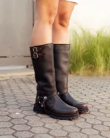 Bota de caña alta confeccionada en cuero color marrón caoba con acabado desgastado. Presenta una suela track robusta, correas con hebillas en la parte superior de la caña y un arnés decorativo con herrajes metálicos en el tobillo.