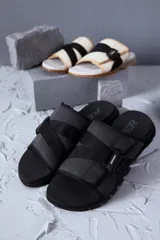 Sandalias tipo slide negras con doble tira de tela acolchada con ajuste de velcro y logo de la marca. Suela anatómica con diseño geométrico.