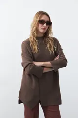 Polera de tejido de punto color marrón, con diseño asimétrico y costura diagonal frontal. Presenta cuello alto, hombros caídos, mangas largas con puños acanalados y ruedo con abertura frontal.