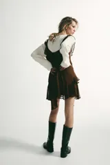 Vestido corto color marrón con escote en pico y tirantes anchos. Presenta un diseño con múltiples volantes en cascada que recorren el frente y el bajo, con un acabado asimétrico.