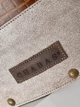 Bolso matero de cuero marrón con textura tipo cocodrilo en la parte superior y cuero liso color beige en la parte inferior. Tiene doble asa de cuero, costuras blancas a la vista y detalles de tachas metálicas. Incluye colgante de cuero y forro interior.